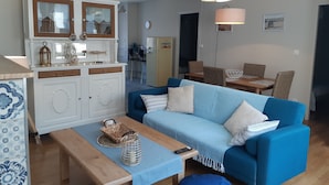 Ein gemütliches Wohnzimmer mit einem blauen Sofa, einem Holztisch und einer Küchenzeile mit einem weißen Schrank und einem Kühlschrank.