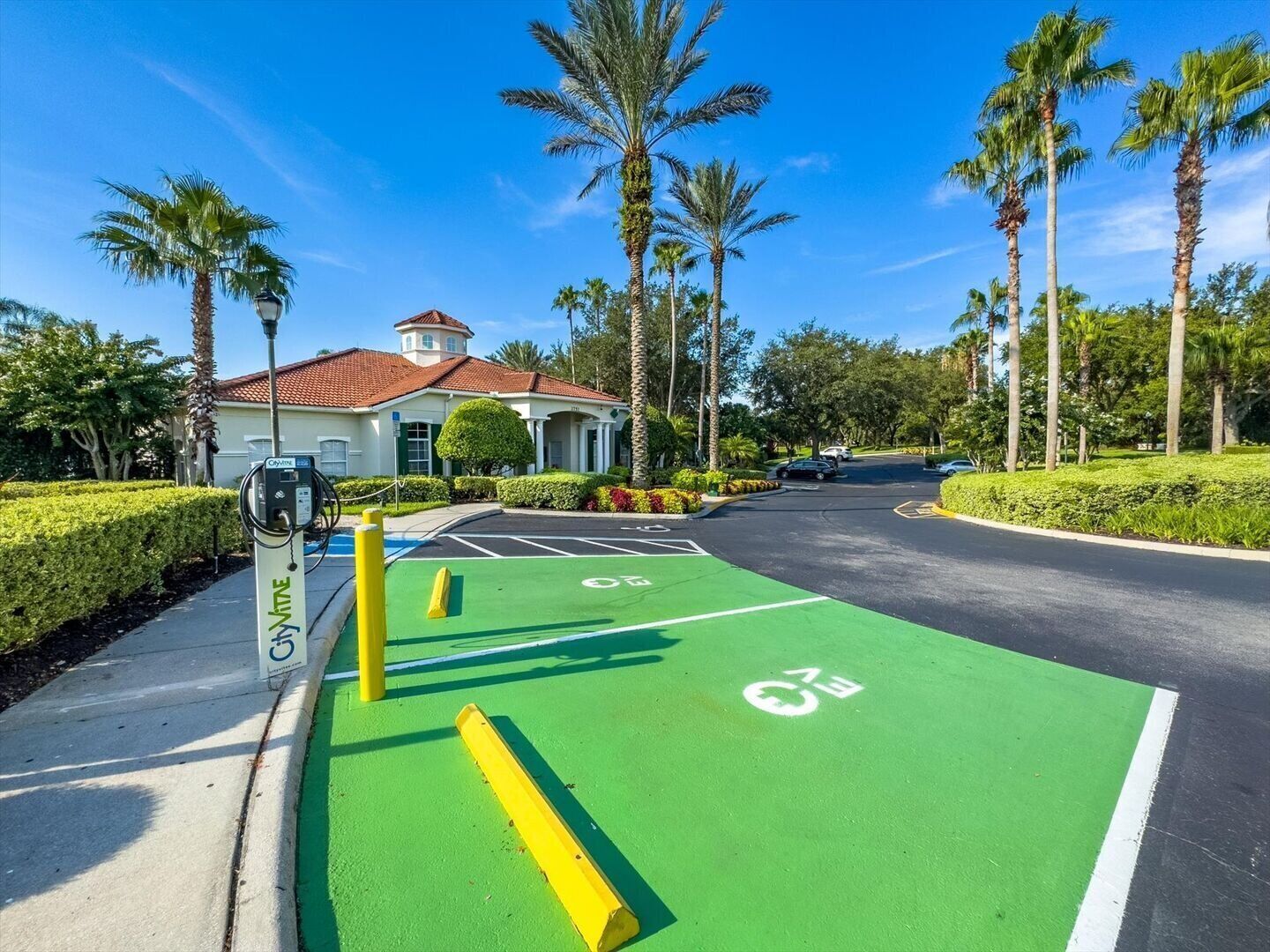 Un espace de stationnement agrémenté d’une piste cyclable verte, d’une borne de recharge et d’un bâtiment dont le toit est recouvert de tuiles rouges.