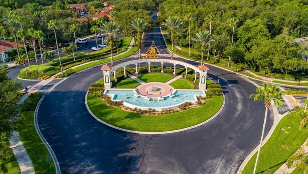 Uma rotatória ajardinada com uma fonte central, cercada por palmeiras e uma estrada.