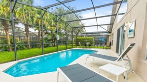 Uma área de piscina com estrutura de vidro, cadeiras de descanso e uma pequena mesa.