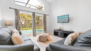Sala de estar moderna com sofás de couro, televisão de tela plana e vista para a piscina.