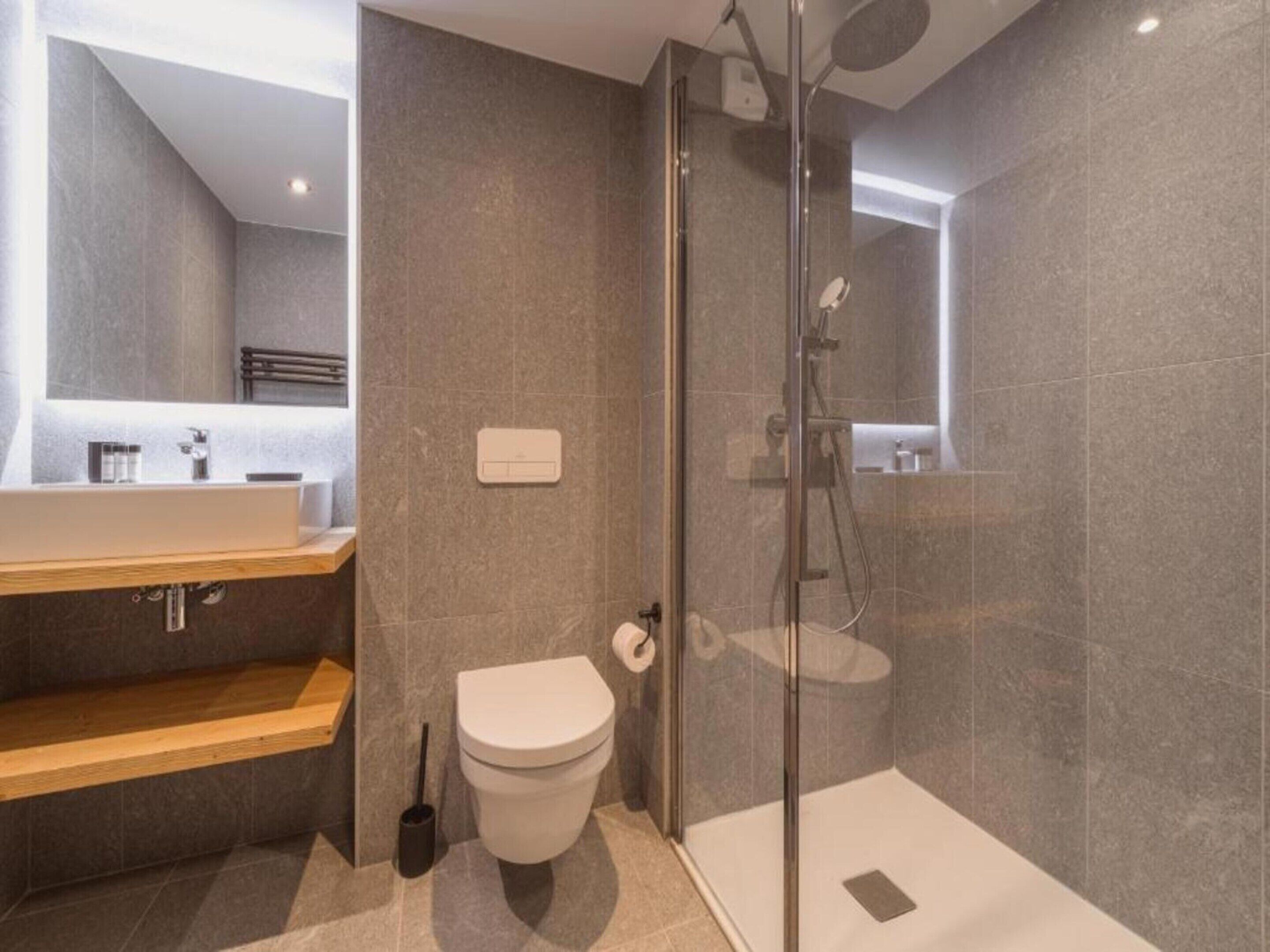 Ein modernes Badezimmer mit einer Duschkabine aus Glas, einer weißen Toilette und einem hölzernen Waschtisch mit Spiegel.