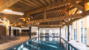 An indoor swimming pool with wooden beams, lounge chairs, and large windows. - Apartment With Mont Blanc View & Spa (Combloux)