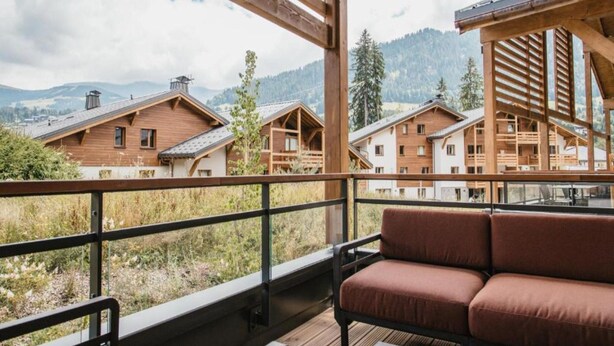 A wooden deck with a sofa and a table, overlooking a mountainous landscape with several wooden buildings. - Apartment With Mont Blanc View & Spa (Combloux)