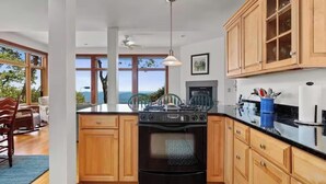Une cuisine moderne avec des meubles en bois, une cuisinière noire et une grande fenêtre donnant sur l’extérieur.