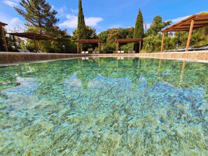 Una piscina cristalina con sillones de descanso y pérgolas de madera.