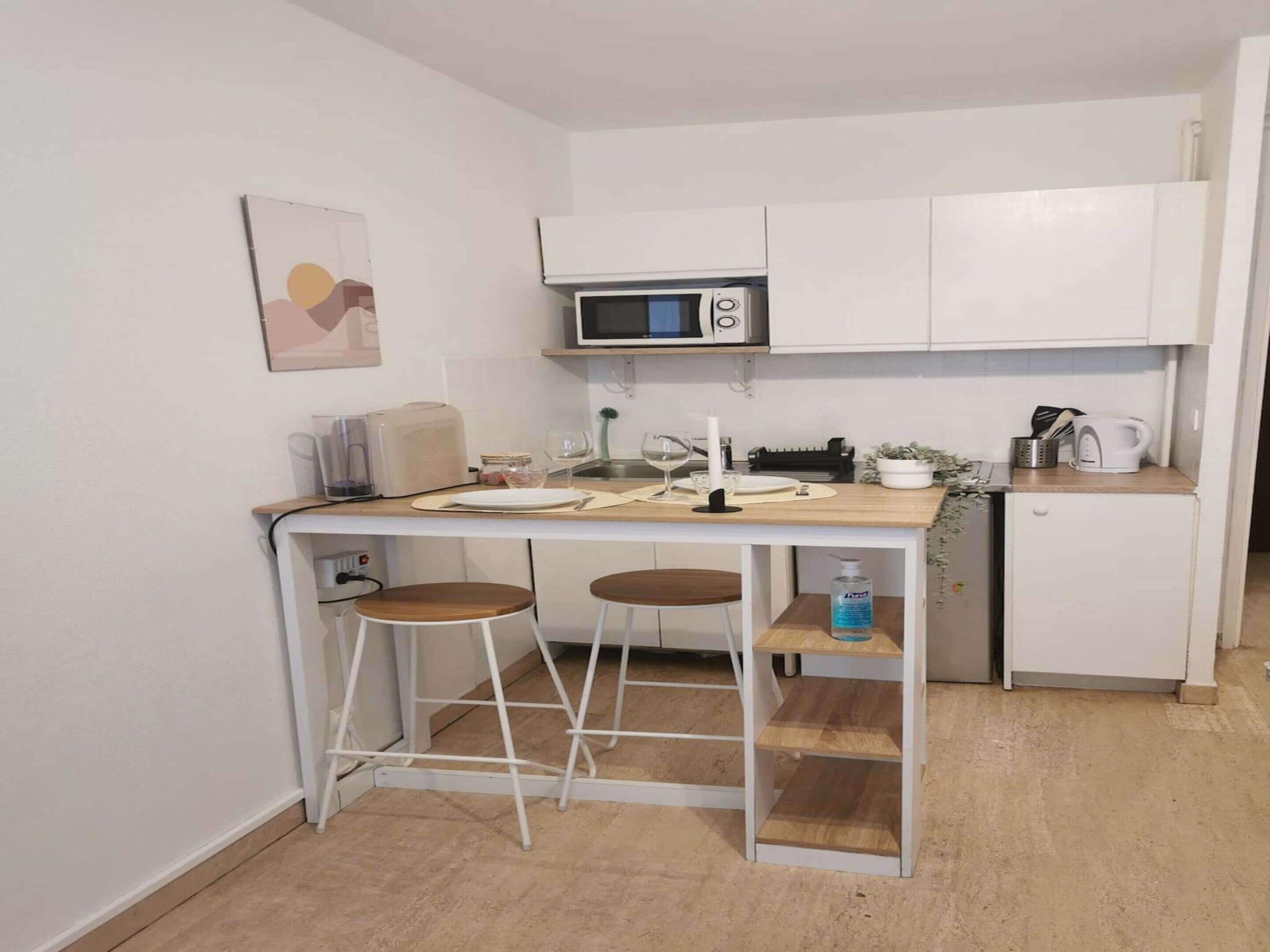 A compact kitchen with a microwave, toaster, and bar stools.