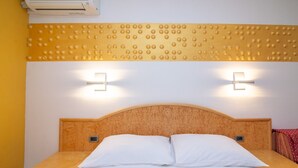 A hotel room with a wooden headboard, two bedside lamps, a bed with white linens, and an air conditioning unit above the bed.
