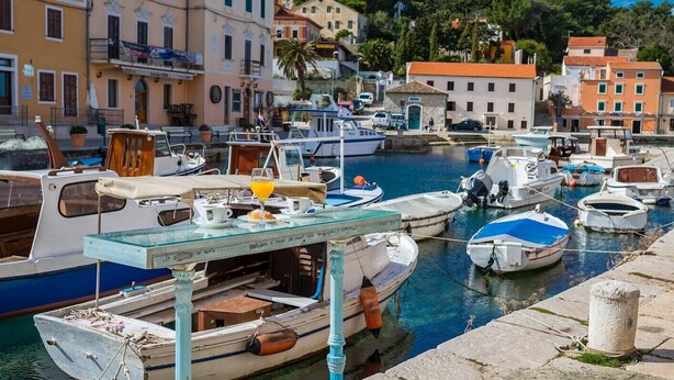 A marina with various boats docked, a glass table with items on it, and buildings in the background.