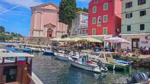 A waterfront area with boats docked, a building with classical architecture, and outdoor seating areas. - Pansion Saturn / Pansion Saturn room 14 (Veli Lošinj)