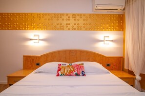 A hotel room with a wooden headboard, two bedside tables, a bed with white bedding, two wall-mounted lights, and an air conditioning unit. - Pansion Saturn / Pansion Saturn soba 25 (Veli Lošinj)