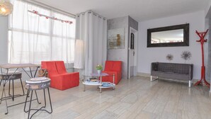 Una sala de estar con sofá, sillón, mesa de centro y una lámpara roja de pie.