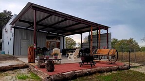 Eine überdachte Terrasse im Freien mit Grill, Sitzgelegenheiten und einem Gebäude mit Metallfassade.