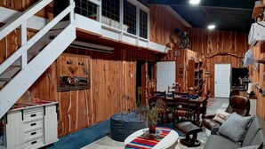 Ein rustikales Interieur mit Treppe, Holzwänden, einer Essecke und einem Wohnbereich inklusive Sofa und Hocker.