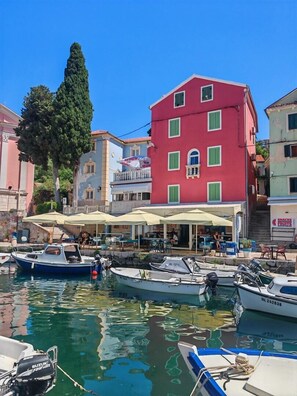 Ein Yachthafen mit vertäuten Booten, ein rotes Gebäude mit grünen Fensterläden und Sitzgelegenheiten im Freien.