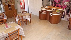 A dining area with wooden tables and chairs, a buffet counter with various food items, and a decorative wall with a floral mural. - Pansion Saturn / Pansion Saturn 15 (Veli Lošinj)