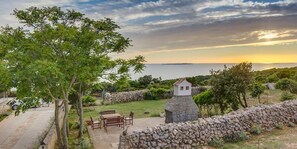 Un muro de piedra, una mesa de madera con sillas y una edificación de piedra con un ventanal pequeño.