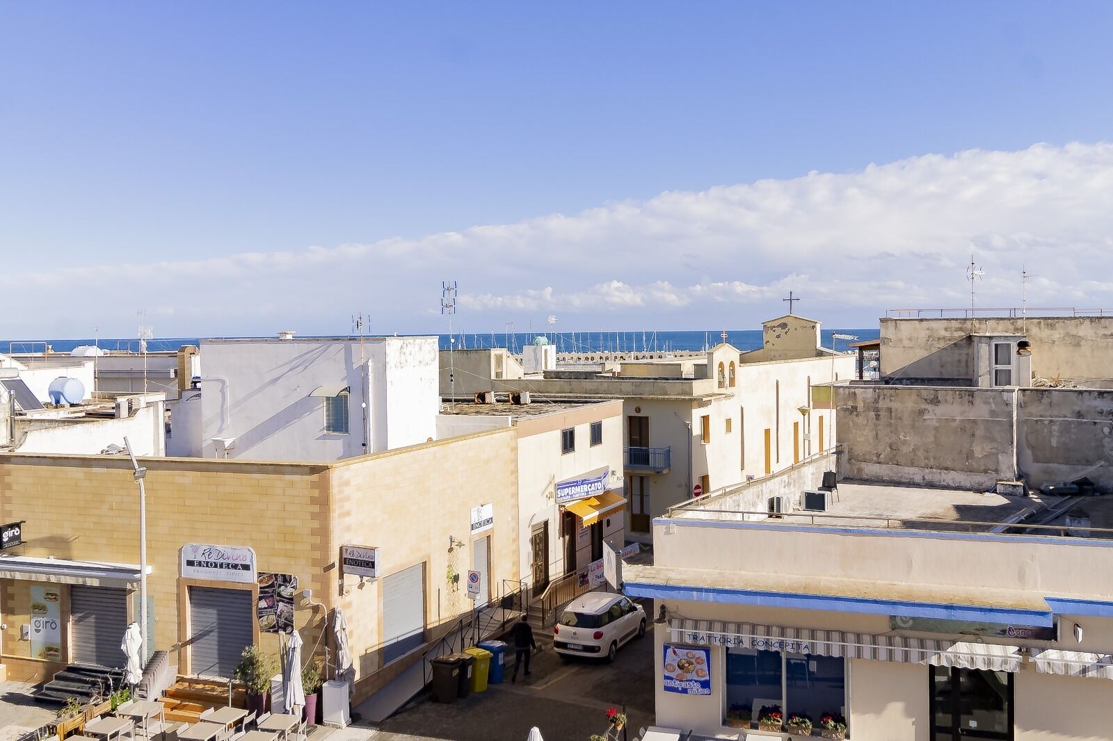 Une ville côtière aux rues étroites, où se côtoient des immeubles d’habitation et des commerces, et d’où l’on peut admirer une vue dégagée sur la mer en arrière-plan.