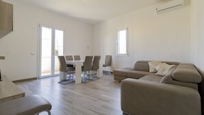 Amplia sala de estar con un conjunto de sofás, una mesa de comedor con sillas y una zona de cocina con mostrador.