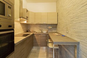 A modern kitchen with a built-in oven, a microwave, a sink, and a bar area with stools. - Madreperla Flat  (San Foca)
