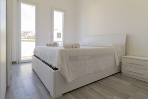 A minimalist bedroom with a bed, a nightstand, and a view through a door. - Madreperla Flat  (San Foca)
