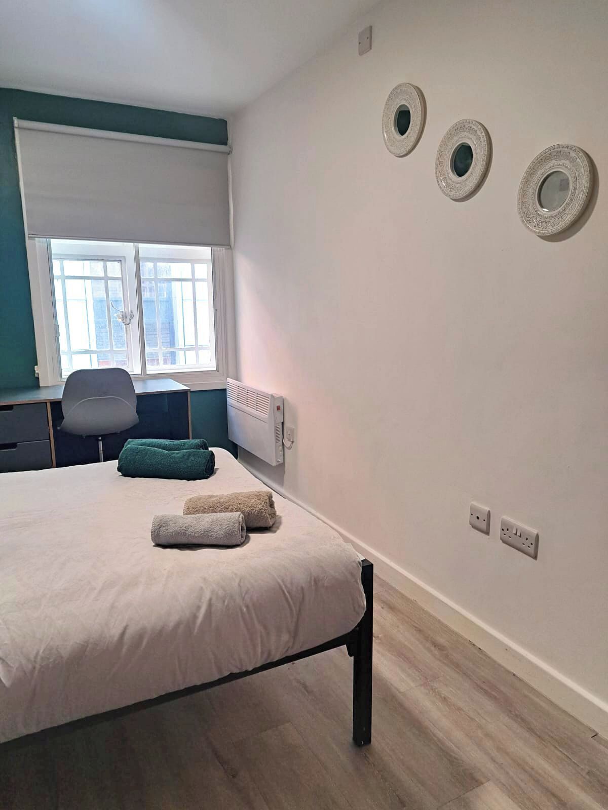 Un dormitorio con cama, escritorio, silla y ventana.