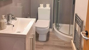 Moderni kylpyhuone, jossa on pesuallas, wc ja lasinen suihkuseinä.