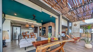 A spacious living area with a wooden bench, a dining table with fruit and wine, and a view of the kitchen and dining area. - Nuju Rentals|1Br Penthouse|Jacuzzi, Cenote & Sauna (Tulum)