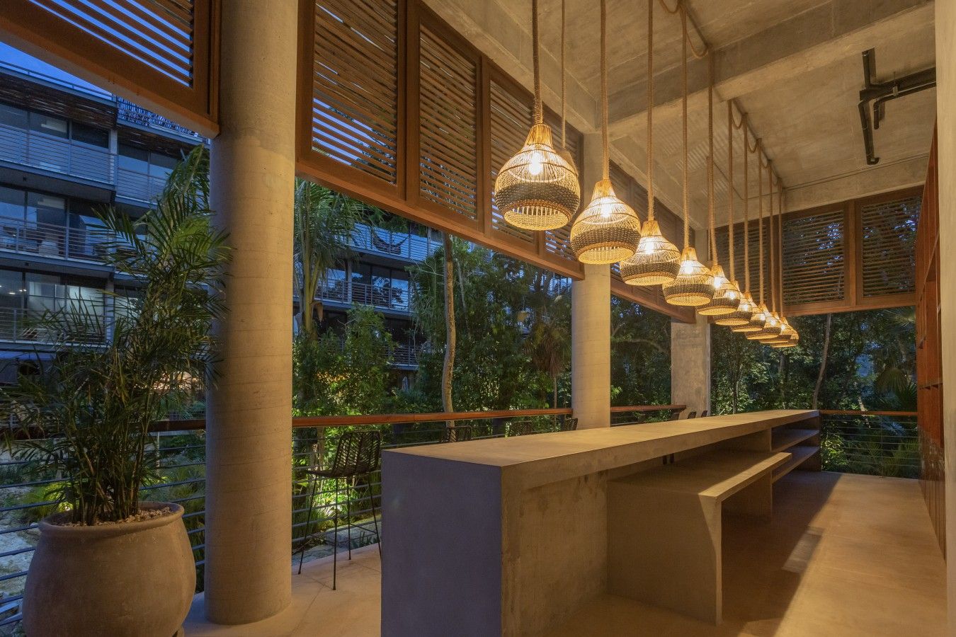 A modern interior with a long bench, large windows, and hanging wicker lamps.