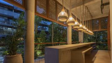 A modern interior with a long bench, large windows, and hanging wicker lamps.