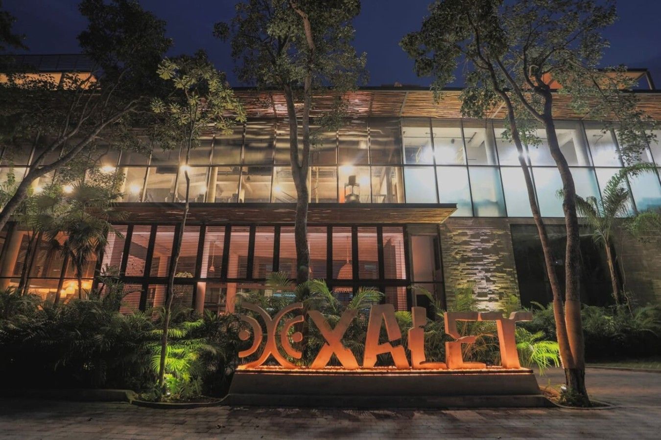 A modern building with a glass facade, surrounded by trees and a well-lit entrance.