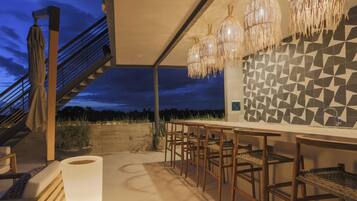 An outdoor bar area with a staircase, wooden chairs, and hanging light fixtures.