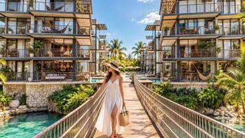 A resort with a wooden bridge connecting two buildings, a pool, and lush greenery.