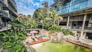 A rooftop pool with a wooden deck and lounge chairs, surrounded by lush greenery and modern buildings. - Nuju Rentals|1Br Penthouse|Jacuzzi, Cenote & Sauna (Tulum)