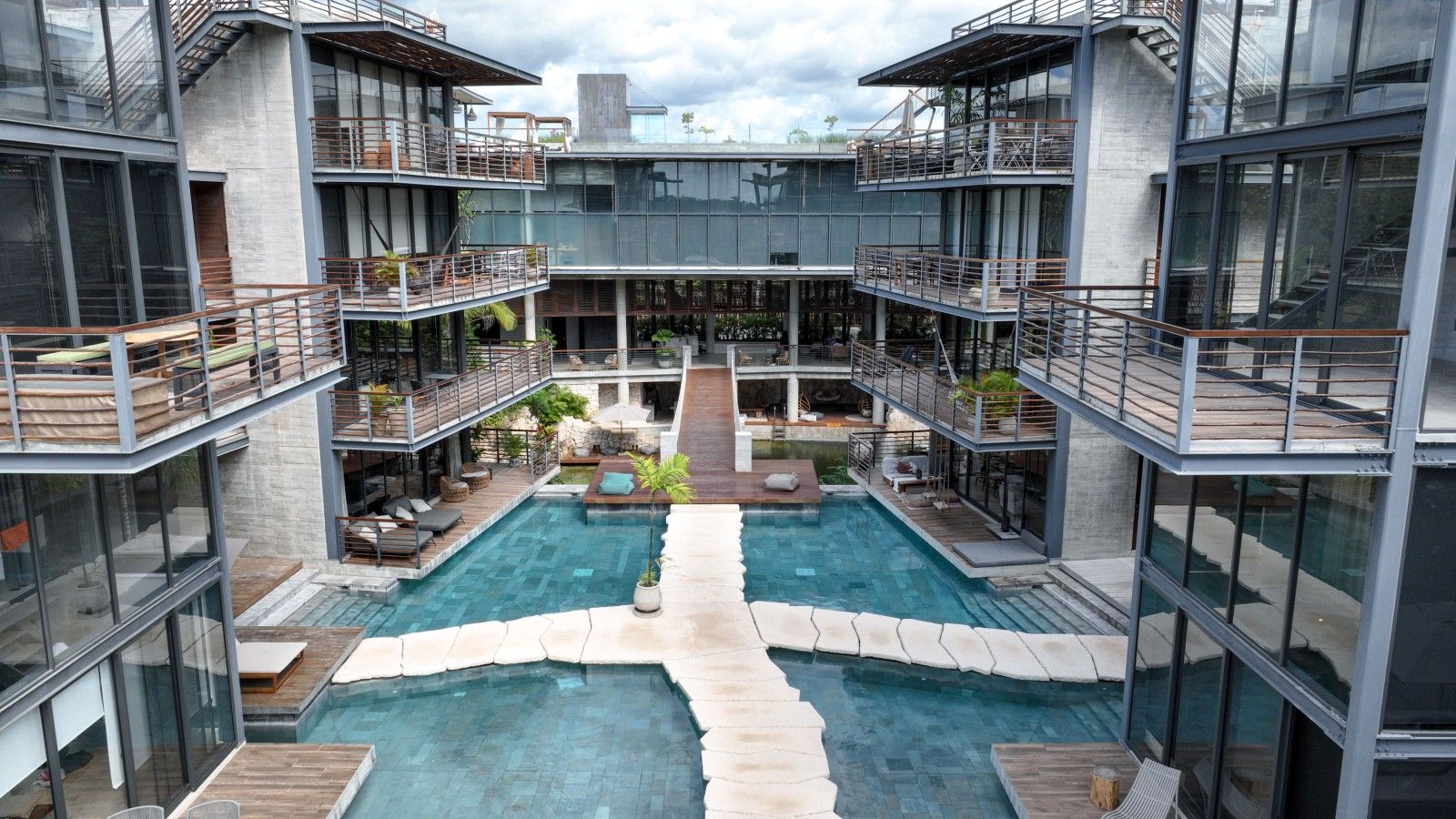 Un bâtiment moderne doté d’une cour intérieure avec une piscine, des espaces de détente en plein air et de nombreux balcons.