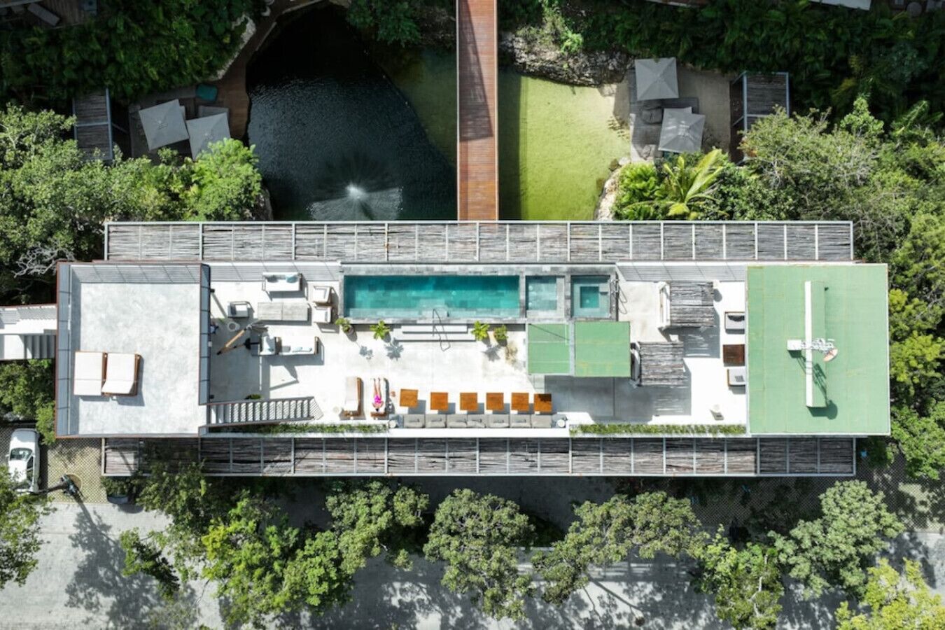 An aerial view of a modern building with a rooftop pool, outdoor seating, and lush greenery.