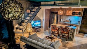 A modern living room with a sofa, a coffee table, a TV, and a kitchen area with a microwave and a sink. - Nuju Rentals|1Br Penthouse|Jacuzzi, Cenote & Sauna (Tulum)