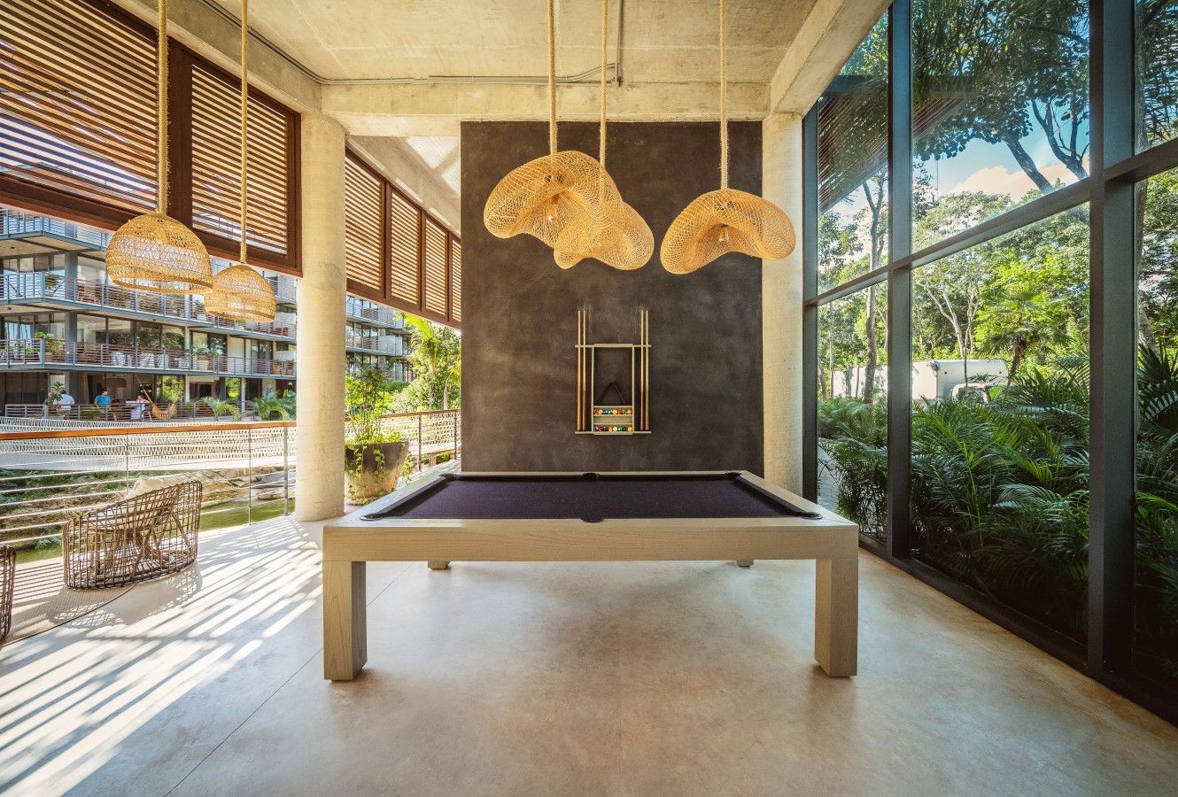 Une table de billard dans une pièce spacieuse, dotée de grandes fenêtres, d’un design moderne au niveau du plafond et offrant une vue sur un balcon.