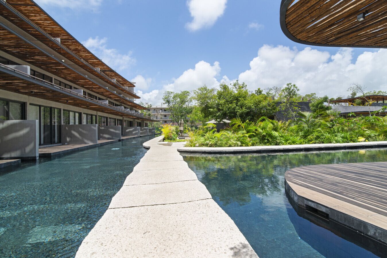 Een modern hotel met een zwembad, terras en weelderige begroeiing.