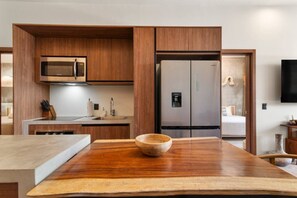 A modern kitchen with wooden cabinets, a stainless steel refrigerator, and a wooden dining table. - Tulum 3BR Swim-Out Condo | 3 King Beds & Private Pool Access (Tulum)