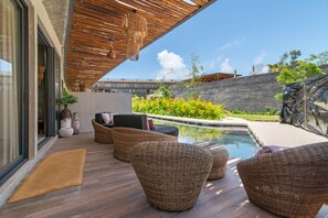A modern outdoor pool area with wicker furniture and a stone wall in the background. - Tulum 3BR Swim-Out Condo | 3 King Beds & Private Pool Access (Tulum)