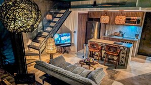 A modern living room with a sofa, a TV, a staircase, and a kitchen area with a microwave and sink. - Nuju Rentals|Penthouse|Private Jacuzzi, Gym&Sauna (Tulum)