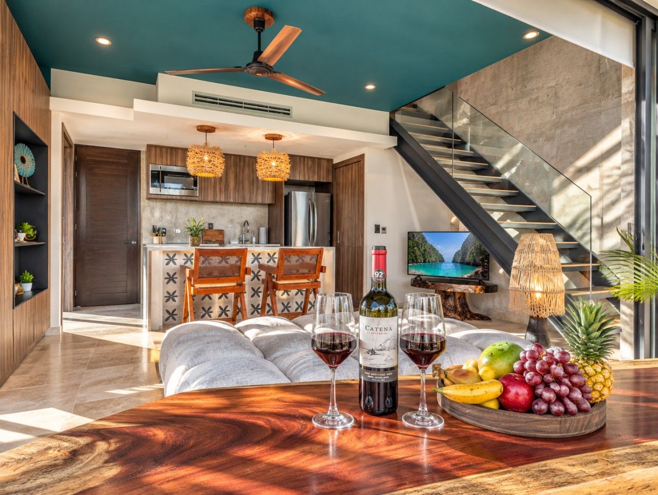 A modern living room with a wooden coffee table, two wine glasses, a bottle of wine, and a fruit bowl.