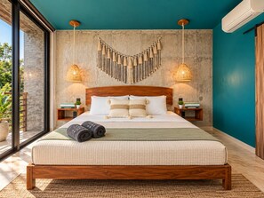 Une chambre moderne avec un grand lit, deux tables de chevet, une décoration murale en macramé et une vue à travers une porte vitrée.
