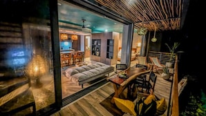 A modern interior with a sofa, dining table, and chairs. There is a kitchen area visible through a glass partition. - Nuju Rentals|Penthouse|Private Jacuzzi, Gym&Sauna (Tulum)