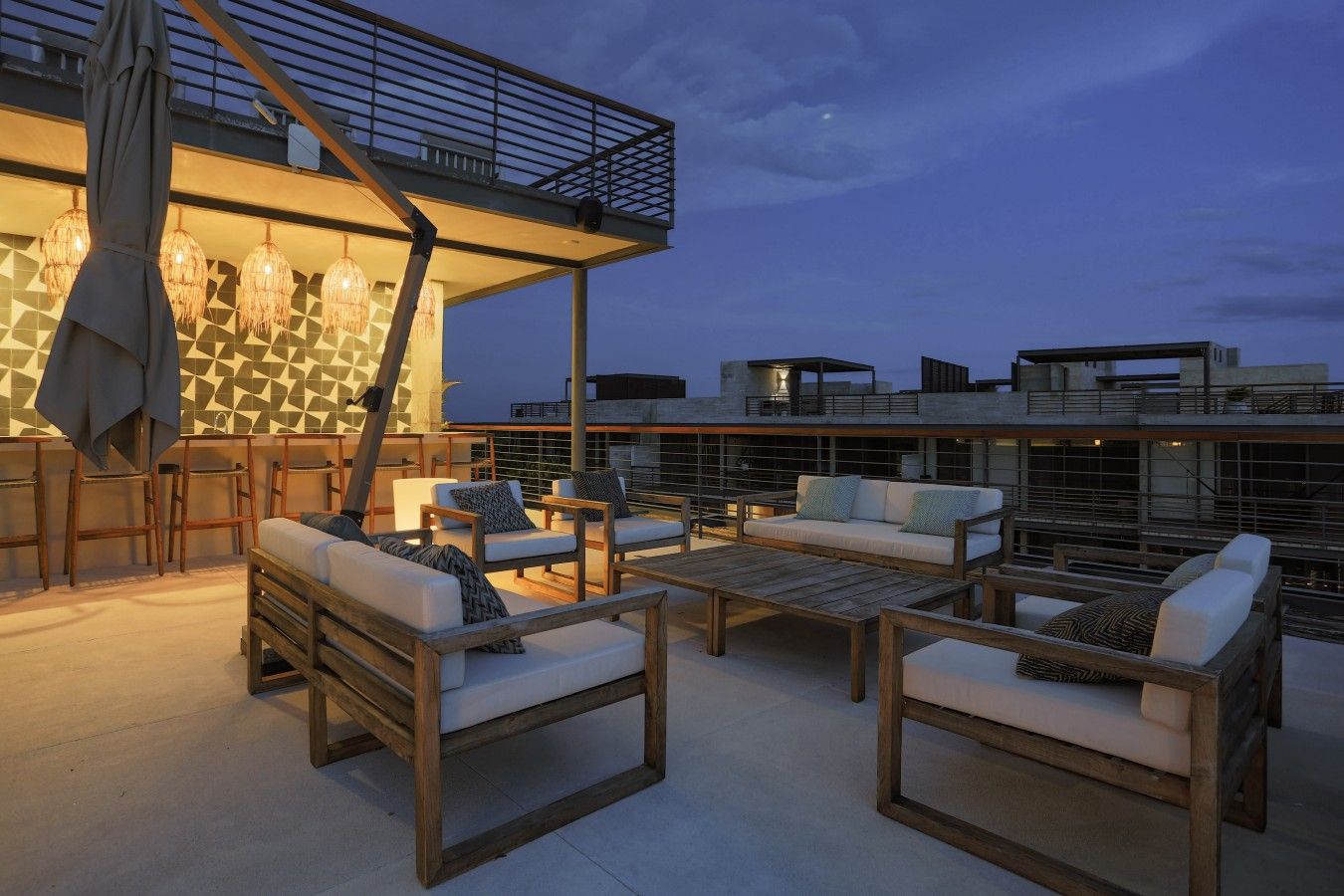 A rooftop terrace with outdoor seating, a geometric patterned wall, and a view of the city skyline at dusk.