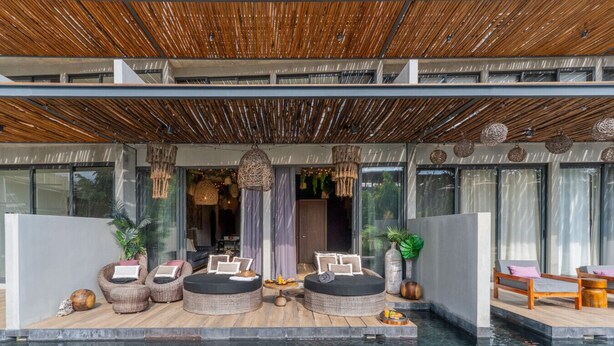 Zona de piscina moderna al aire libre con mobiliario de mimbre, una lámpara colgante y vistas a la piscina.