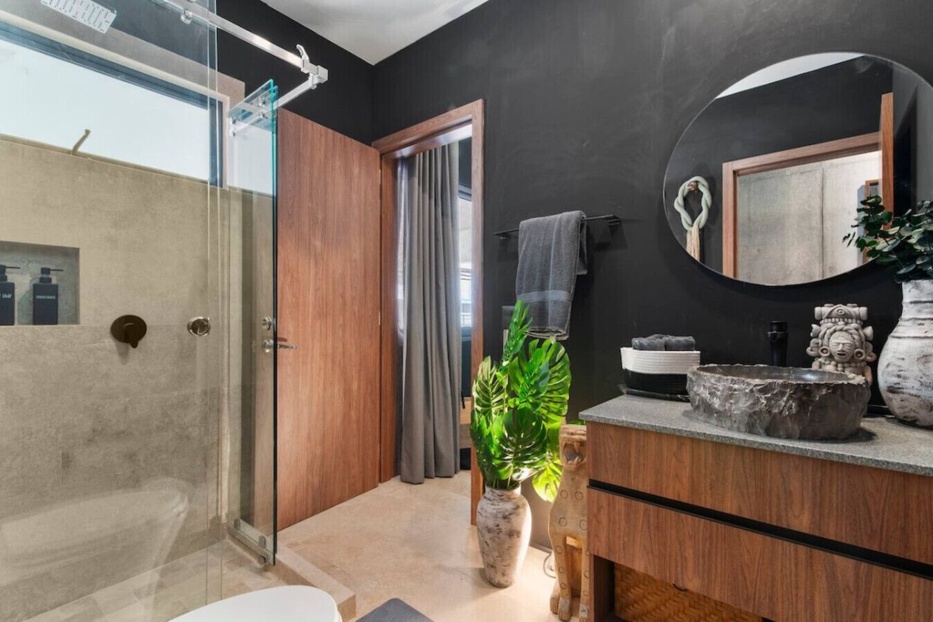 A modern bathroom with a glass shower enclosure, a wooden vanity, a large mirror, and a potted plant.