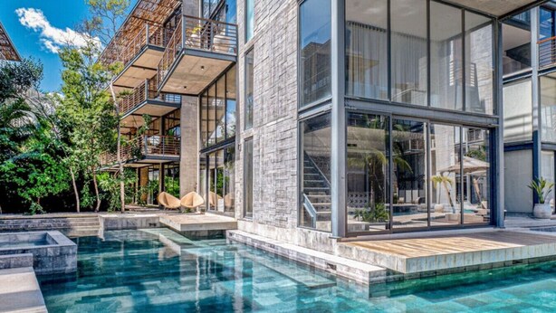 Ein modernes Haus mit Schwimmbad, großen Fenstern und Sitzgelegenheit im Freien.