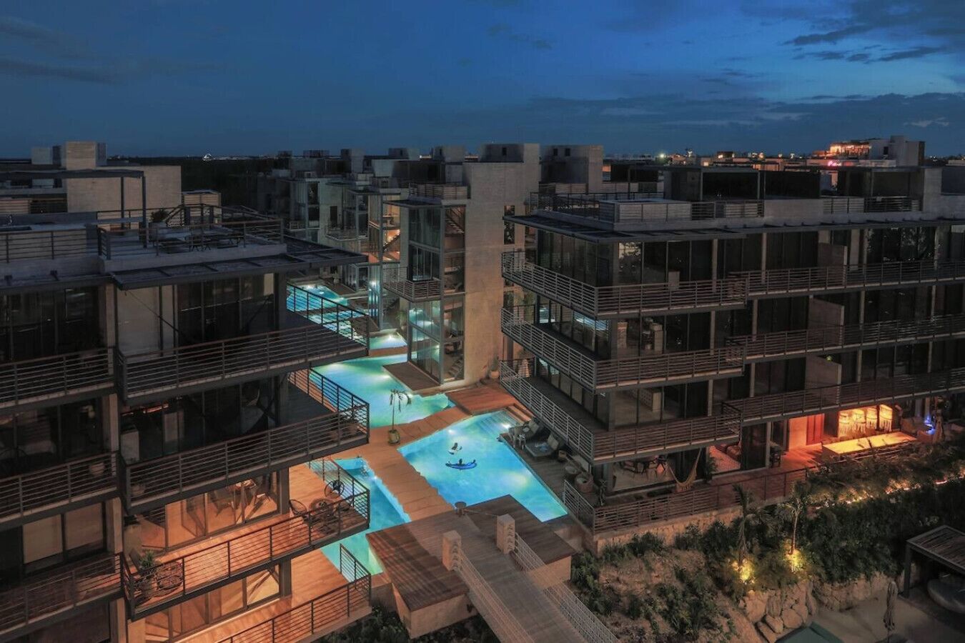 A modern multi-story building with a rooftop pool and outdoor seating areas.